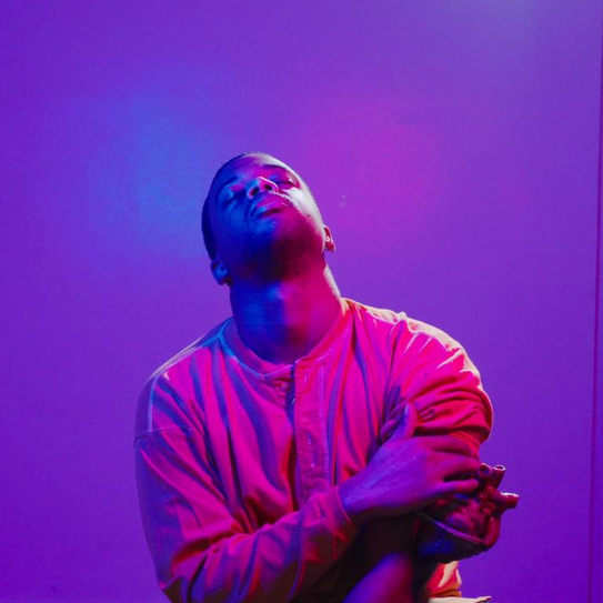 Resident Artist Jovon Outlaw in pink light with a heart sculpture on his sleeve against a purple background